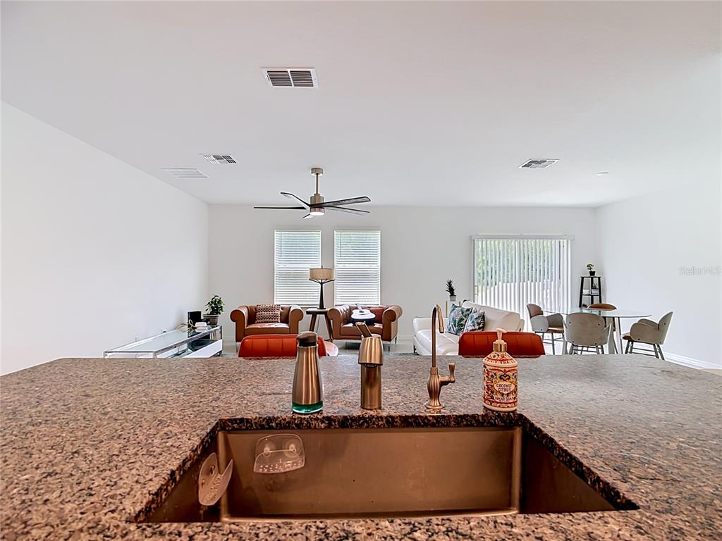 A kitchen island with a granite countertop and stainless steel sink overlooks an open-concept living area — 1633 RED LOOP, LAKELAND, FL