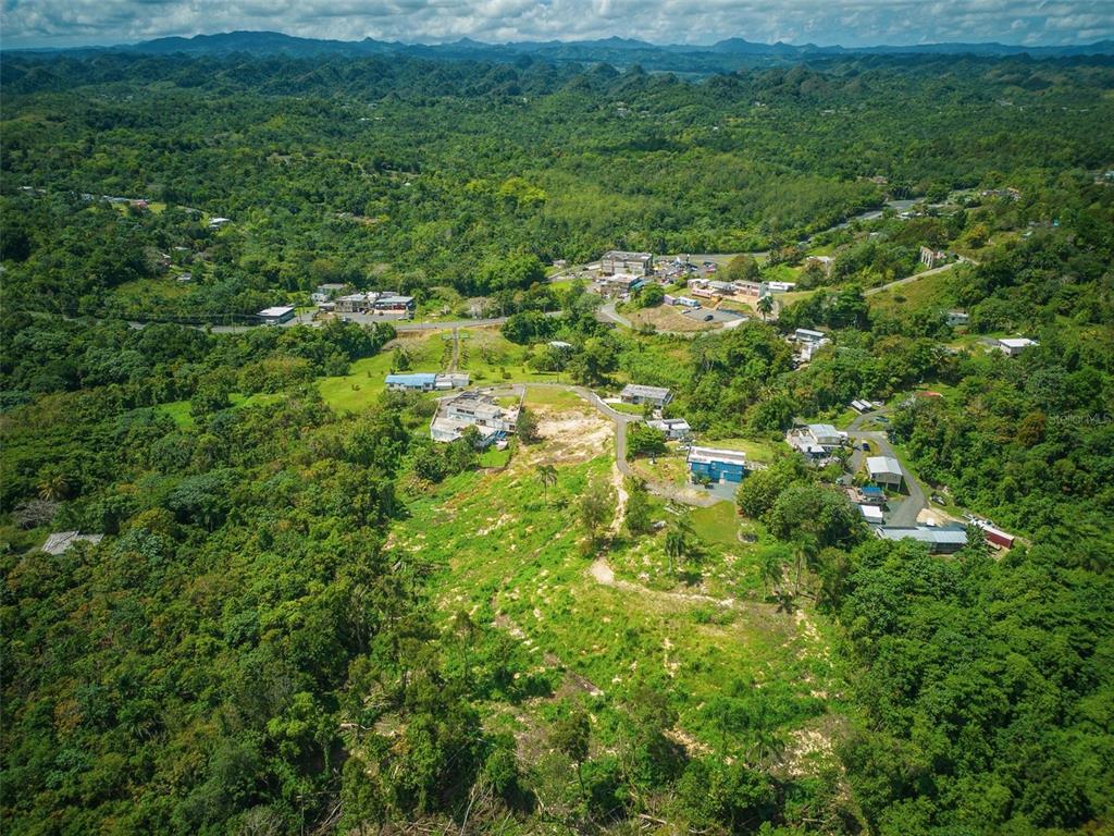 An aerial view shows houses scattered across a lush, hilly landscape with dense green forest — PR-129 KM QUEBRADA, CAMUY, PR
