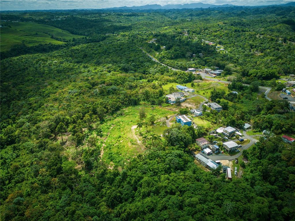 An aerial view shows a rural landscape with scattered houses nestled among dense green forests — PR-129 KM QUEBRADA, CAMUY, PR