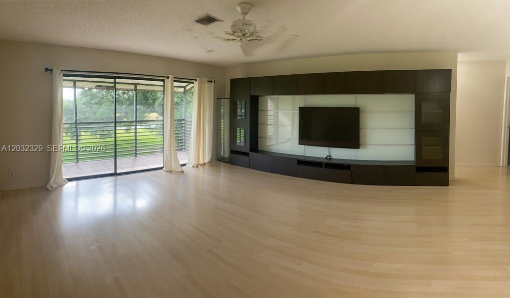 A spacious living room features light wood flooring, a large dark media unit, and sliding doors — 125 S Laurel Dr # 506, Margate FL 33063, MARGATE, FL