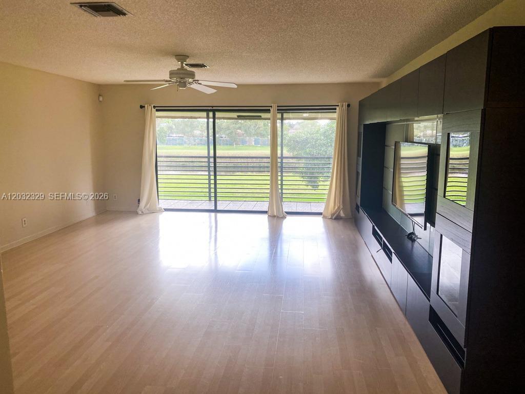 A living room features light wood flooring, a ceiling fan, and a large dark media unit — 125 S Laurel Dr # 506, Margate FL 33063, MARGATE, FL