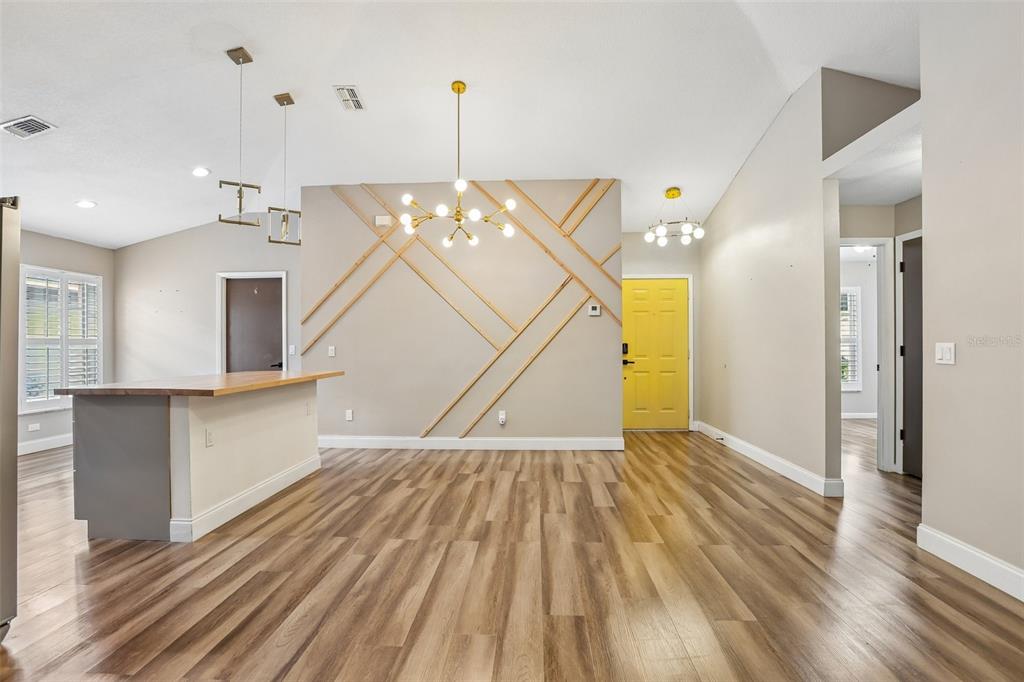A living room features wood-look flooring, a geometric accent wall, and a bright yellow door — 8711 BUSCH OAKS STREET, TAMPA, FL