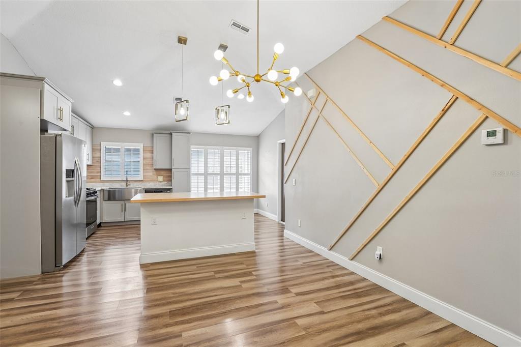 A kitchen and dining area featuring a wood-topped island, modern chandelier, and geometric wall molding — 8711 BUSCH OAKS STREET, TAMPA, FL