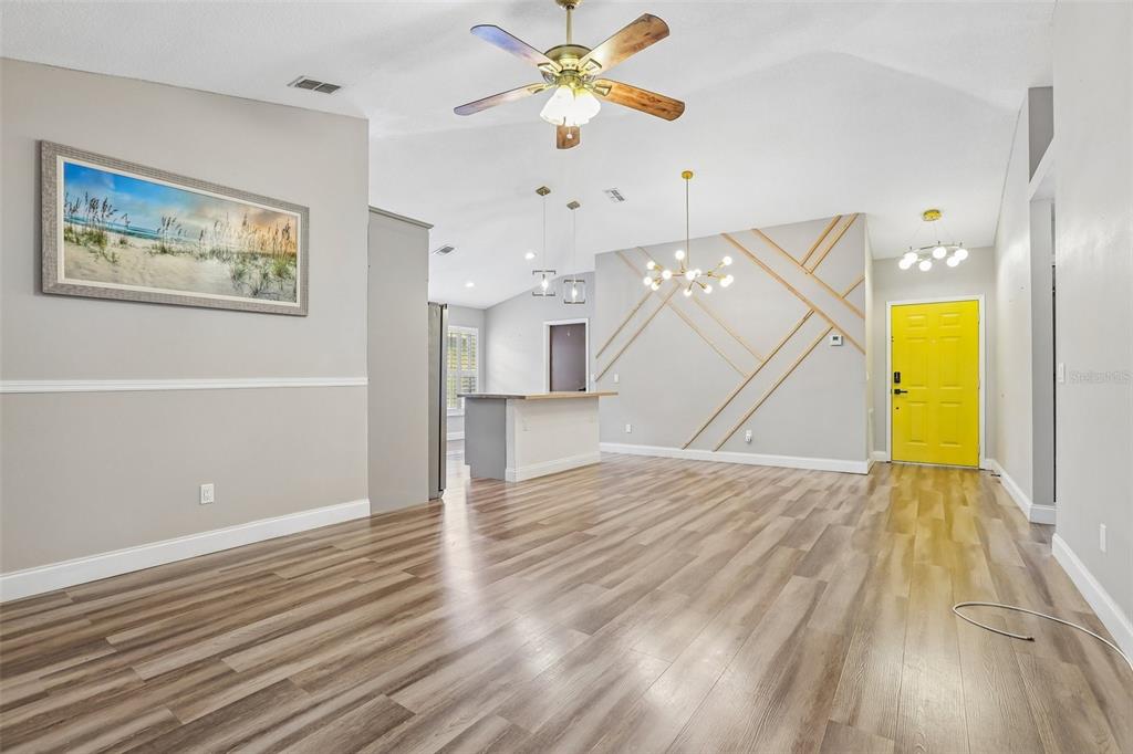 An open-concept living area features wood-look flooring, a yellow front door, and geometric wall molding — 8711 BUSCH OAKS STREET, TAMPA, FL