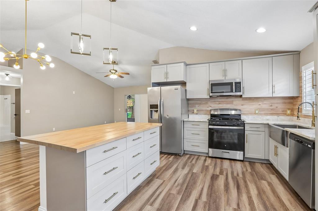 A kitchen features white cabinets, a wood-topped island, stainless steel appliances, and wood-look flooring — 8711 BUSCH OAKS STREET, TAMPA, FL