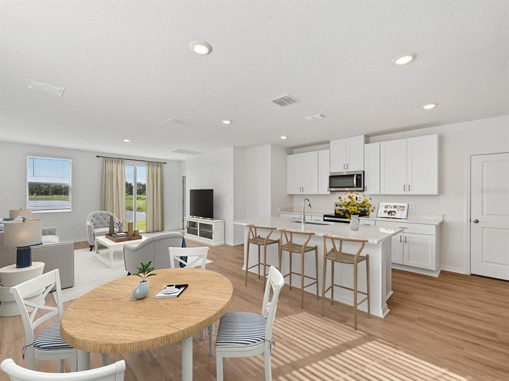 An open-concept kitchen and living area features white cabinetry, a kitchen island, and wood flooring — 1495 BREKEY WAY, ZEPHYRHILLS, FL