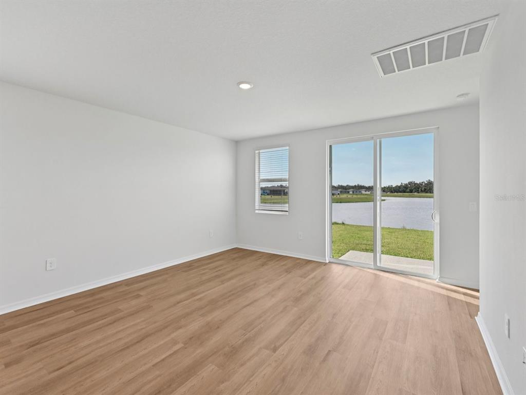 An empty room with light wood-look flooring, white walls, a sliding glass door, and water views — 1495 BREKEY WAY, ZEPHYRHILLS, FL
