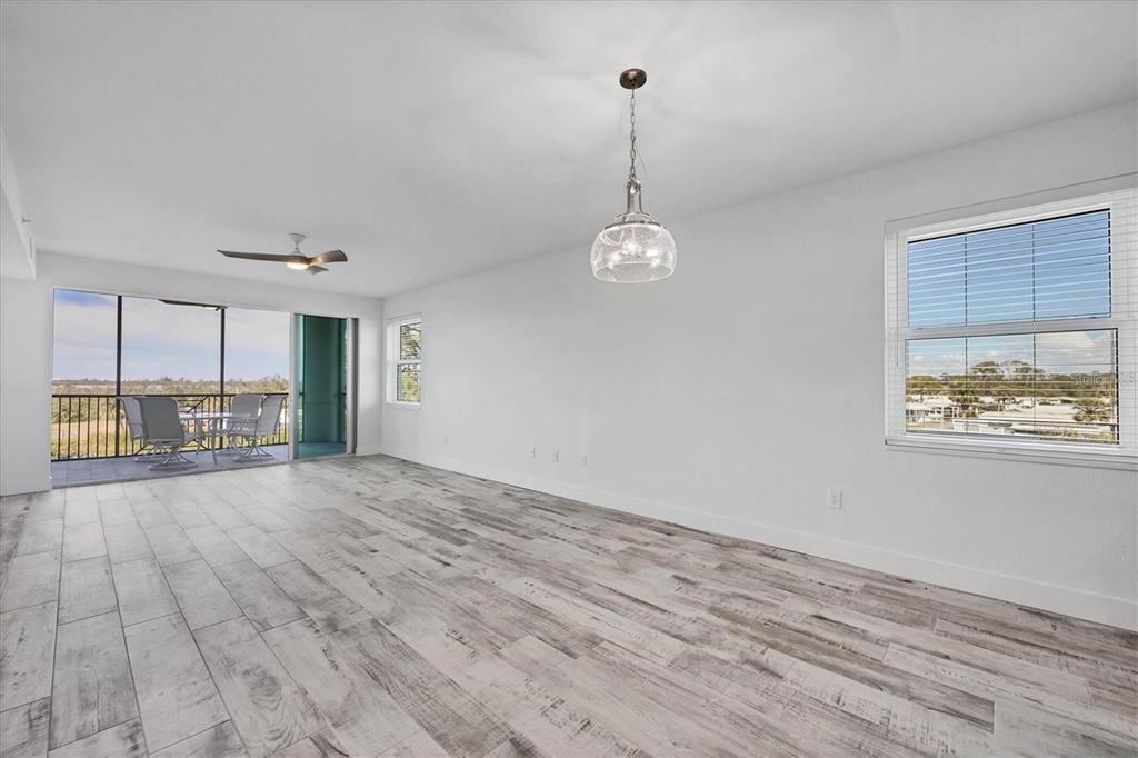 An empty room features light wood-look tile flooring, a pendant light, and a screened balcony — 9203 GRIGGS ROAD UNIT 204, ENGLEWOOD, FL