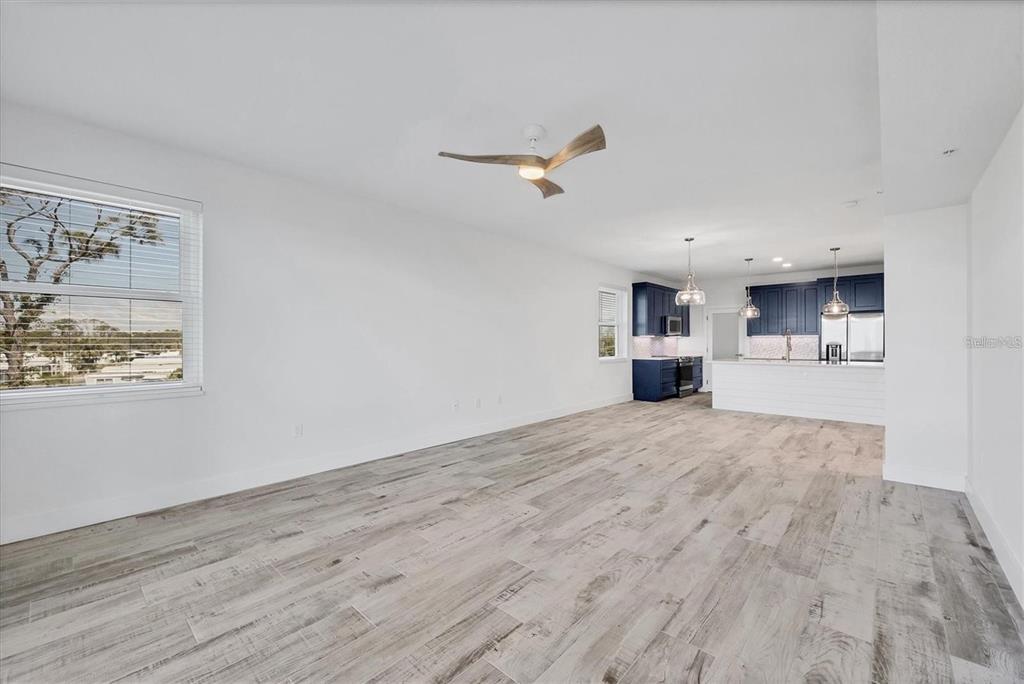 An open-concept living area features light wood-look tile floors, white walls, and a blue kitchen — 9203 GRIGGS ROAD UNIT 204, ENGLEWOOD, FL