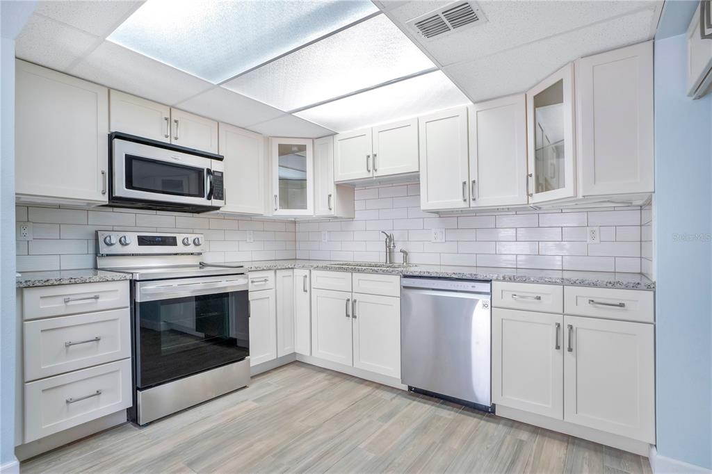 A kitchen with white cabinets, stainless steel appliances, granite countertops, and a white subway tile backsplash — 5656 ROYAL PINE BOULEVARD UNIT 27, ORLANDO, FL