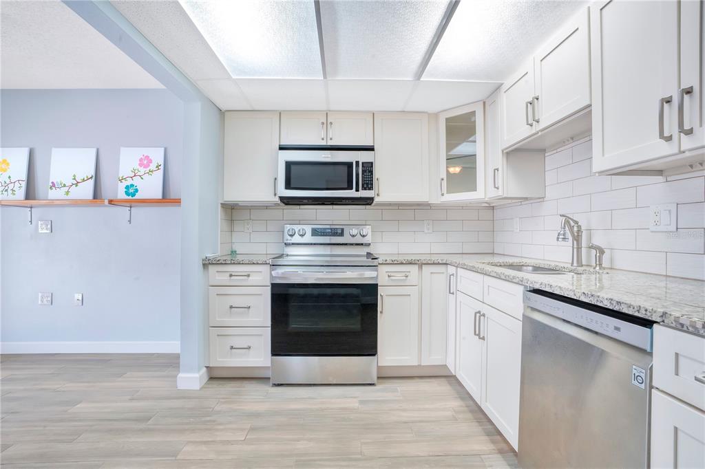 A kitchen features white cabinets, stainless steel appliances, granite countertops, and light wood-look flooring — 5656 ROYAL PINE BOULEVARD UNIT 27, ORLANDO, FL