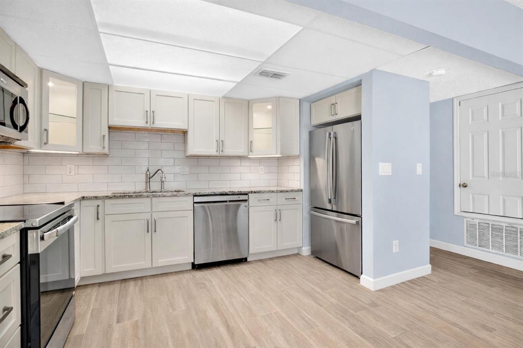 A kitchen with white cabinets, stainless steel appliances, a subway tile backsplash, and wood-look flooring — 5656 ROYAL PINE BOULEVARD UNIT 27, ORLANDO, FL