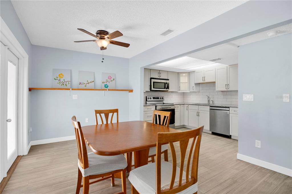 A dining area with a wooden table and chairs opens into a white kitchen — 5656 ROYAL PINE BOULEVARD UNIT 27, ORLANDO, FL