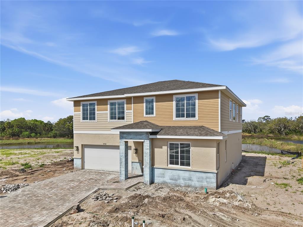 A two-story house with tan siding and a stone-accented entryway sits on a dirt lot — 14510 BANKS COURT, PARRISH, FL
