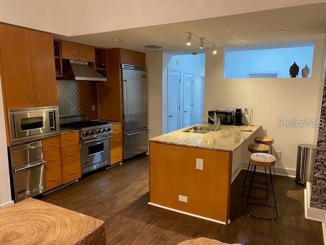 A kitchen features wood cabinets, stainless steel appliances, a granite island, and dark wood flooring — 1208 E KENNEDY BOULEVARD UNIT 825E, TAMPA, FL