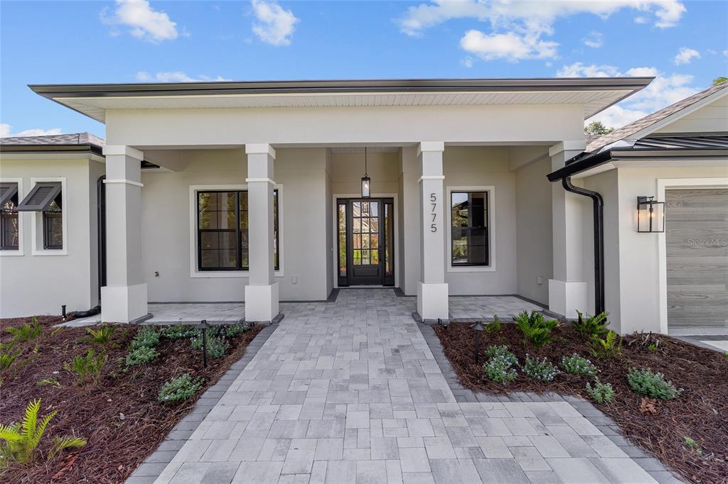 A modern house exterior features a covered entryway with stone pillars and a paved walkway — 5775 SW 43RD PLACE, OCALA, FL