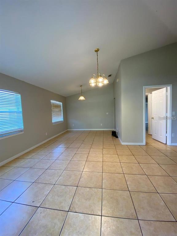 An empty room features beige tile flooring, two windows with blinds, and two hanging chandeliers — 502 BLACKBIRD LANE UNIT A, POINCIANA, FL