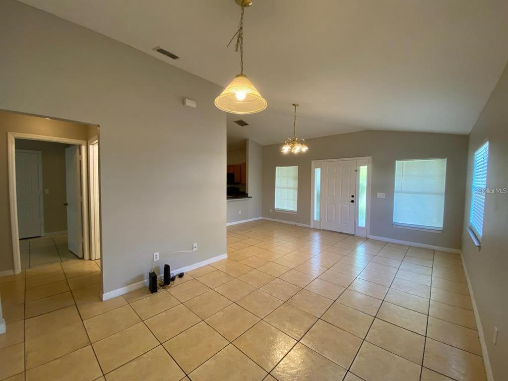 An open-concept living area features beige tile flooring, neutral walls, and two hanging light fixtures — 502 BLACKBIRD LANE UNIT A, POINCIANA, FL