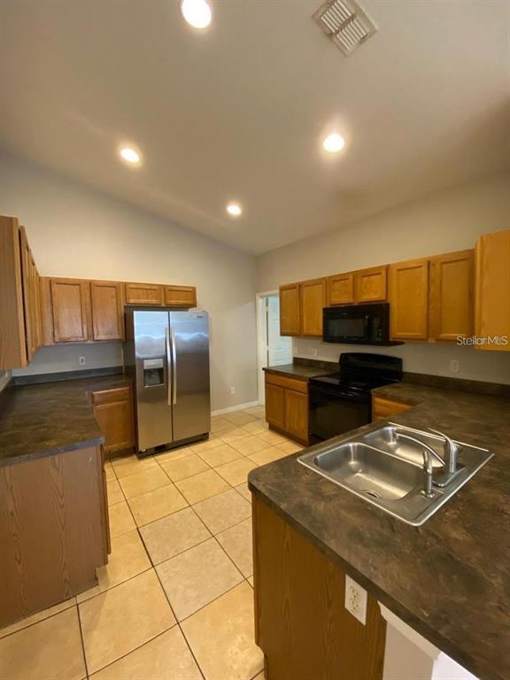 A kitchen features wood cabinets, dark countertops, stainless steel appliances, and light-colored tile flooring — 502 BLACKBIRD LANE UNIT A, POINCIANA, FL