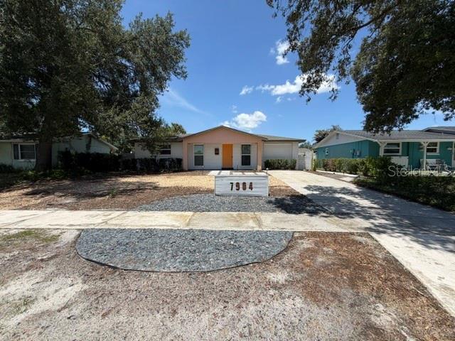 A single-story house with a light-colored exterior, an orange front door, and a driveway — 7904 WOODVINE CIRCLE, TAMPA, FL