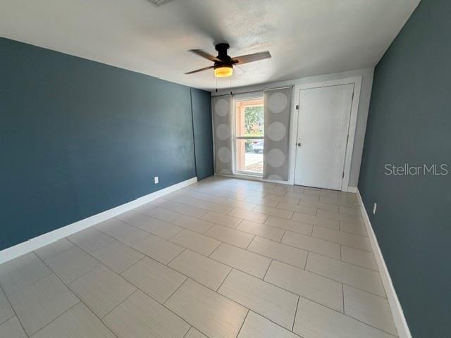 An empty room features dark blue walls, light tile flooring, a ceiling fan, and a door — 7904 WOODVINE CIRCLE, TAMPA, FL