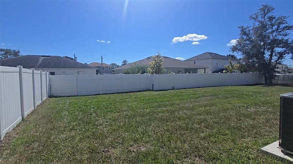 A grassy backyard features a white vinyl privacy fence and views of neighboring houses — 410 DANUBE DRIVE, POINCIANA, FL