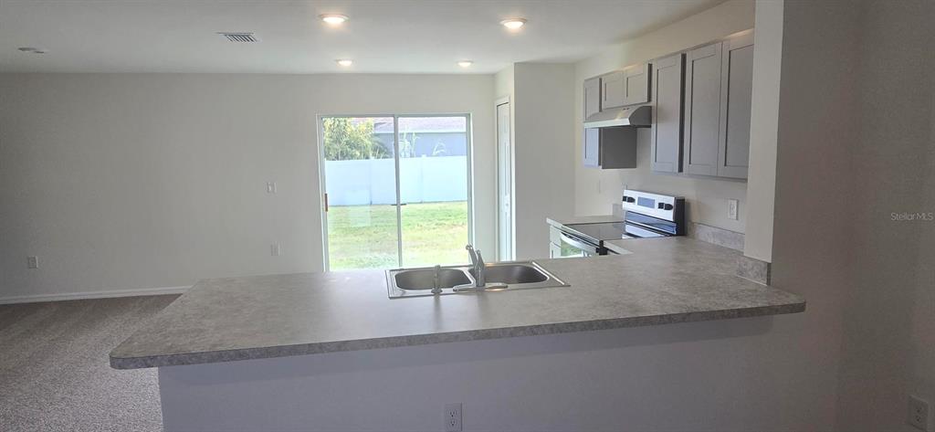 A kitchen with gray cabinets, a laminate countertop, and a sink overlooking a sliding door — 410 DANUBE DRIVE, POINCIANA, FL
