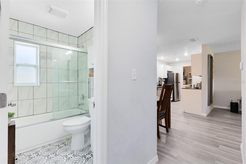 A bathroom with patterned tile flooring and a glass-enclosed tub overlooks a nearby kitchen area — 2190 PATTERSON AVENUE, ORLANDO, FL