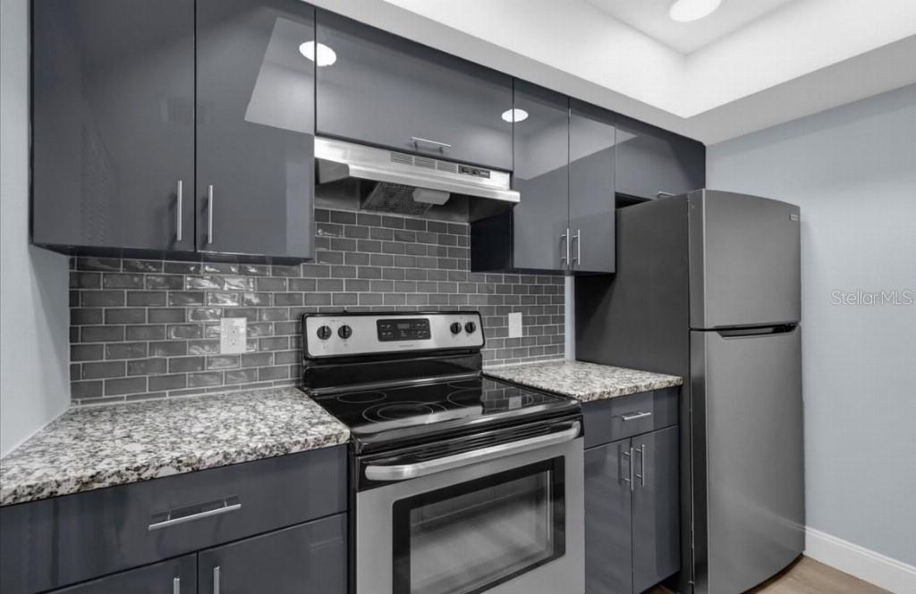 A kitchen features gray glossy cabinets, granite countertops, a subway tile backsplash, and stainless appliances — 321 BOBBY JONES ROAD UNIT 321, SARASOTA, FL