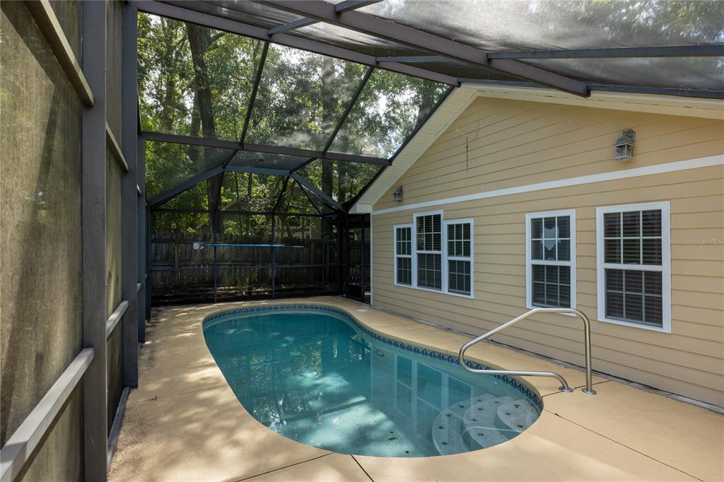 A screened-in patio features a small swimming pool with steps and a metal handrail — 11624 NW 13TH LANE, GAINESVILLE, FL