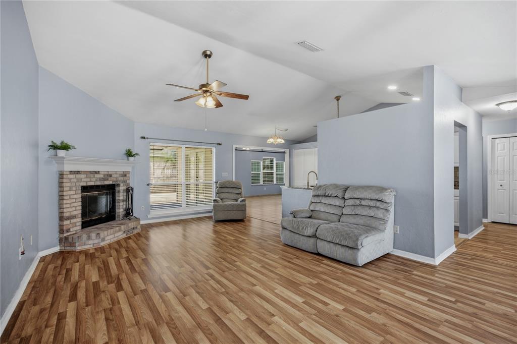 A living room features light blue walls, wood-look flooring, a brick fireplace, and vaulted ceilings — 11624 NW 13TH LANE, GAINESVILLE, FL