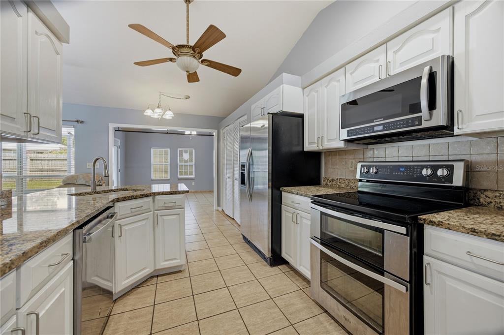 A kitchen features white cabinets, granite countertops, stainless steel appliances, and tile flooring — 11624 NW 13TH LANE, GAINESVILLE, FL