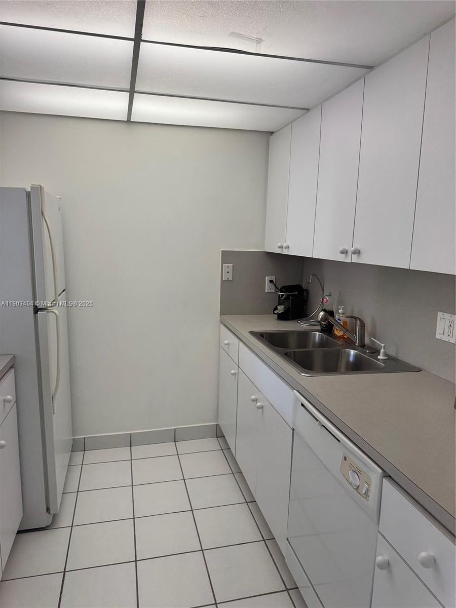 A galley kitchen features white cabinets, a double-basin sink, and white tiled flooring — 14401 N Kendall Dr # 303N, Miami FL 33186, MIAMI, FL