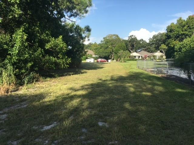 A grassy, undeveloped lot is bordered by trees and a chain-link fence — 3910 DUNN DRIVE, SARASOTA, FL