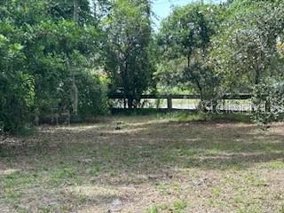 A grassy, partially shaded lot with trees and a wooden fence in the background — 3910 DUNN DRIVE, SARASOTA, FL