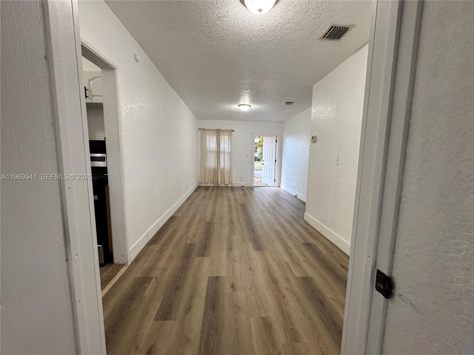 A long, narrow room features white walls, light wood-look flooring, and an open exterior door — 748 NE 127th St, North Miami FL 33161, NORTH MIAMI, FL