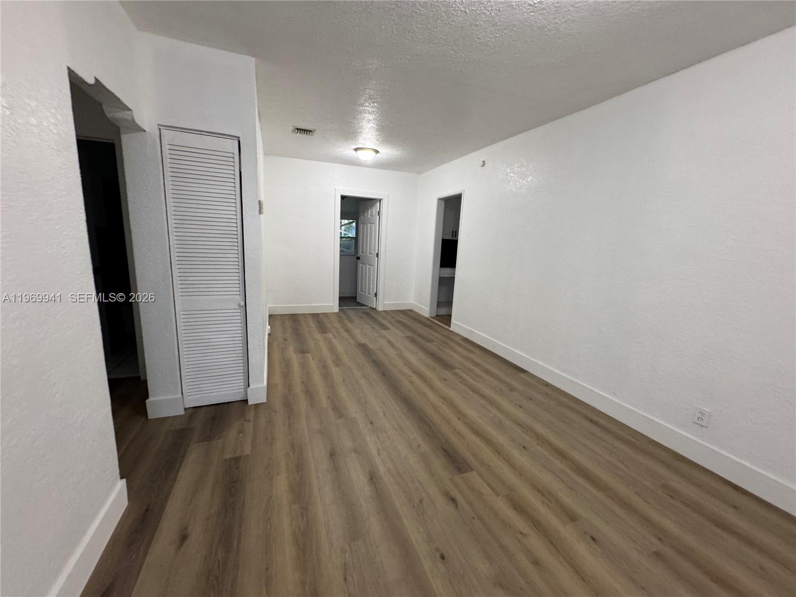 An empty room features white walls, wood-look flooring, a louvered closet door, and two doorways — 748 NE 127th St, North Miami FL 33161, NORTH MIAMI, FL