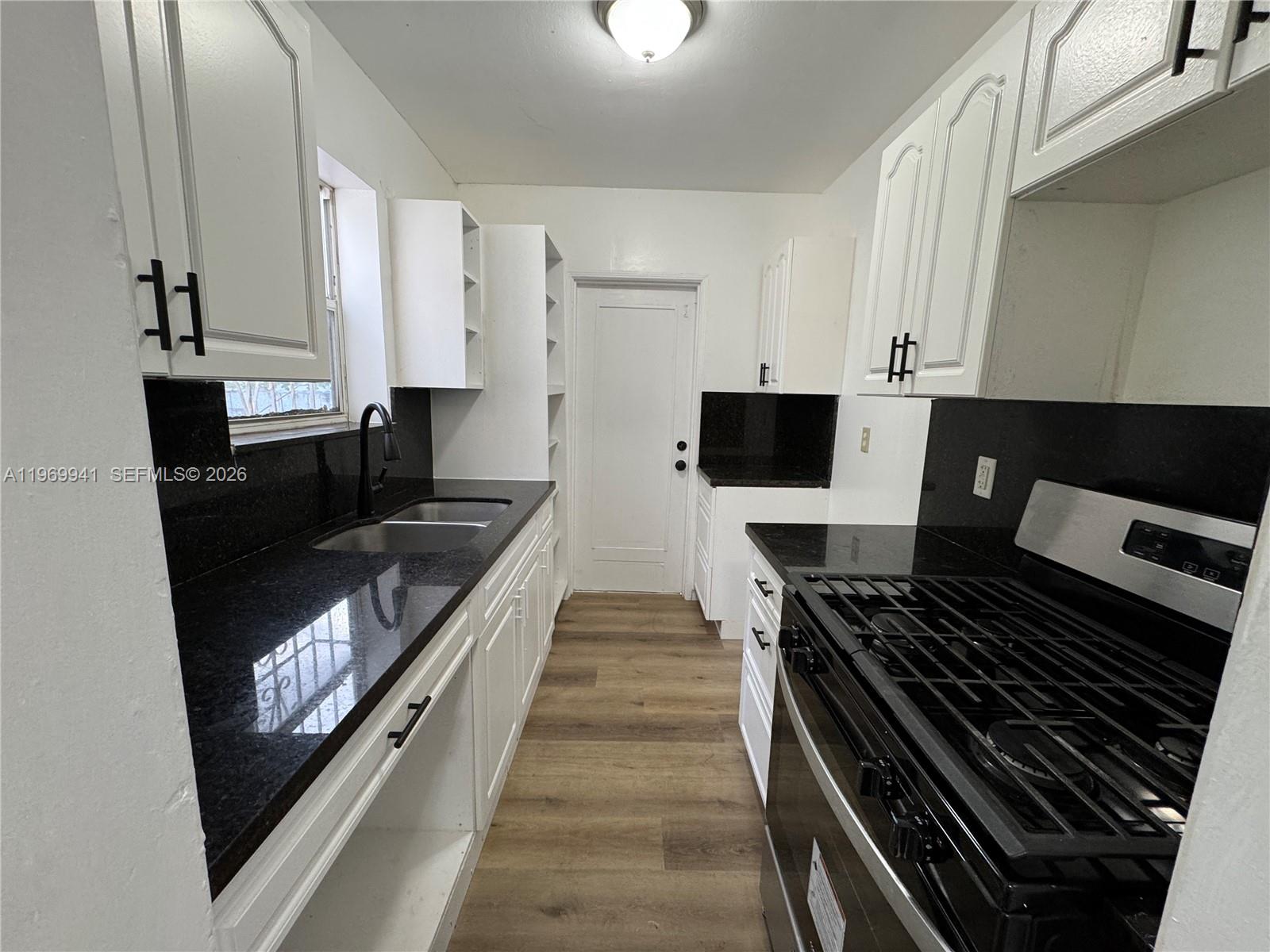 A galley kitchen features white cabinets, black countertops, and a stainless steel gas range — 748 NE 127th St, North Miami FL 33161, NORTH MIAMI, FL