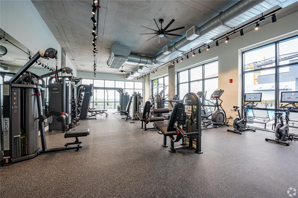 A modern gym features exercise equipment, exposed ductwork, concrete ceilings, and large floor-to-ceiling windows — 221 MAIN STREET N UNIT PH 1612, ST PETERSBURG, FL