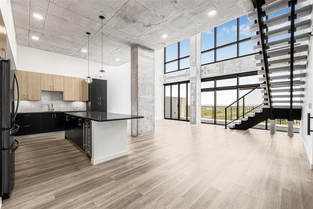 A modern kitchen and living area with concrete ceilings, large windows, and a floating staircase — 221 MAIN STREET N UNIT PH 1612, ST PETERSBURG, FL