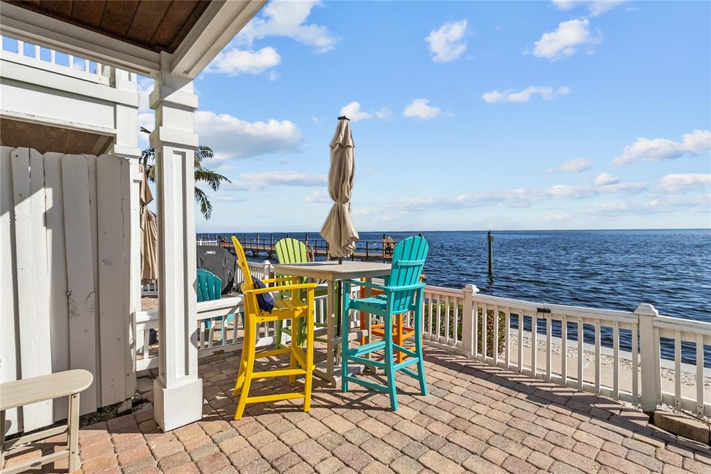 A patio with colorful chairs and a table overlooks a body of water and pier — 5026 COQUINA KEY DRIVE SE UNIT 5026, ST PETERSBURG, FL