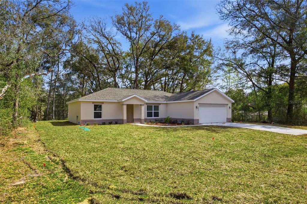 A single-story house with a beige exterior, a two-car garage, and a grassy front yard — 14095 SE 27TH COURT, SUMMERFIELD, FL