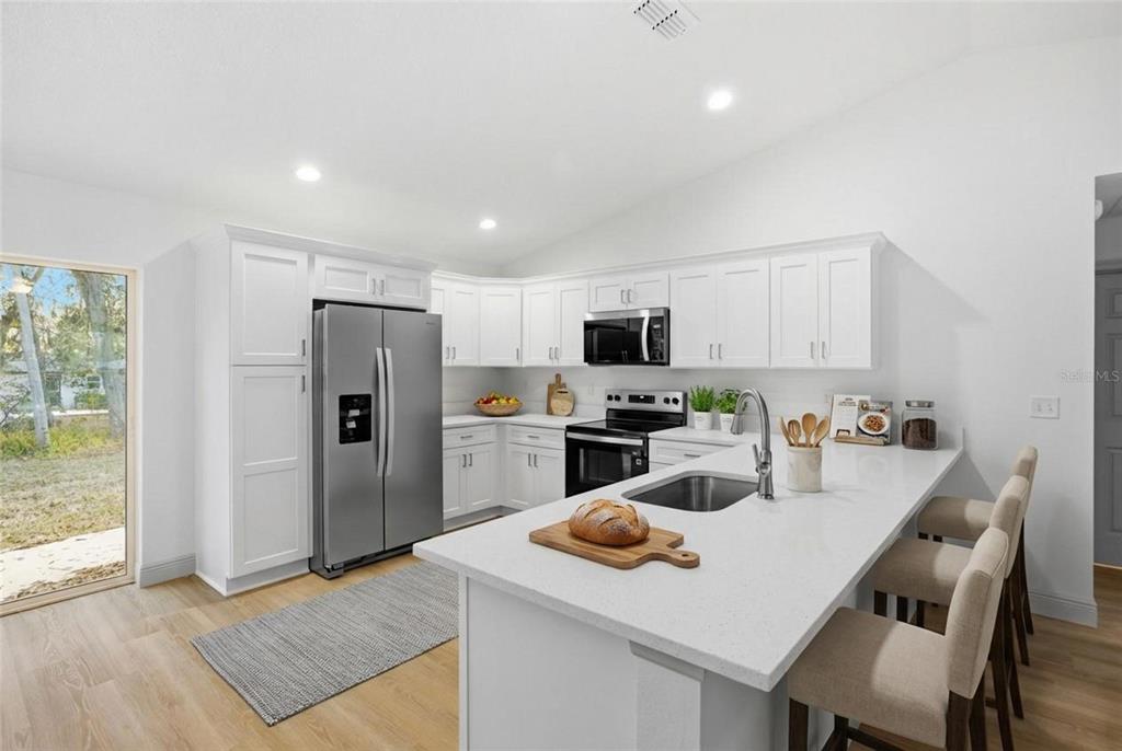 A modern kitchen features white cabinetry, stainless steel appliances, a quartz island, and light flooring — 14095 SE 27TH COURT, SUMMERFIELD, FL