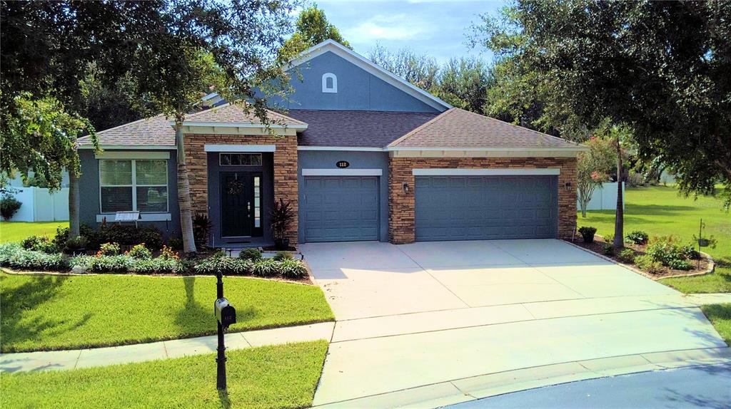 A single-story house with a stone facade, gray siding, and a three-car garage — 112 PECORRI COURT, AUBURNDALE, FL