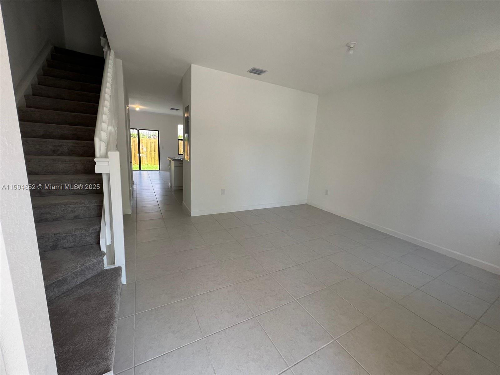A living area with tile flooring and carpeted stairs leading to an upper level — 875 NE 211TH ST # 0, Miami FL 33179, MIAMI, FL