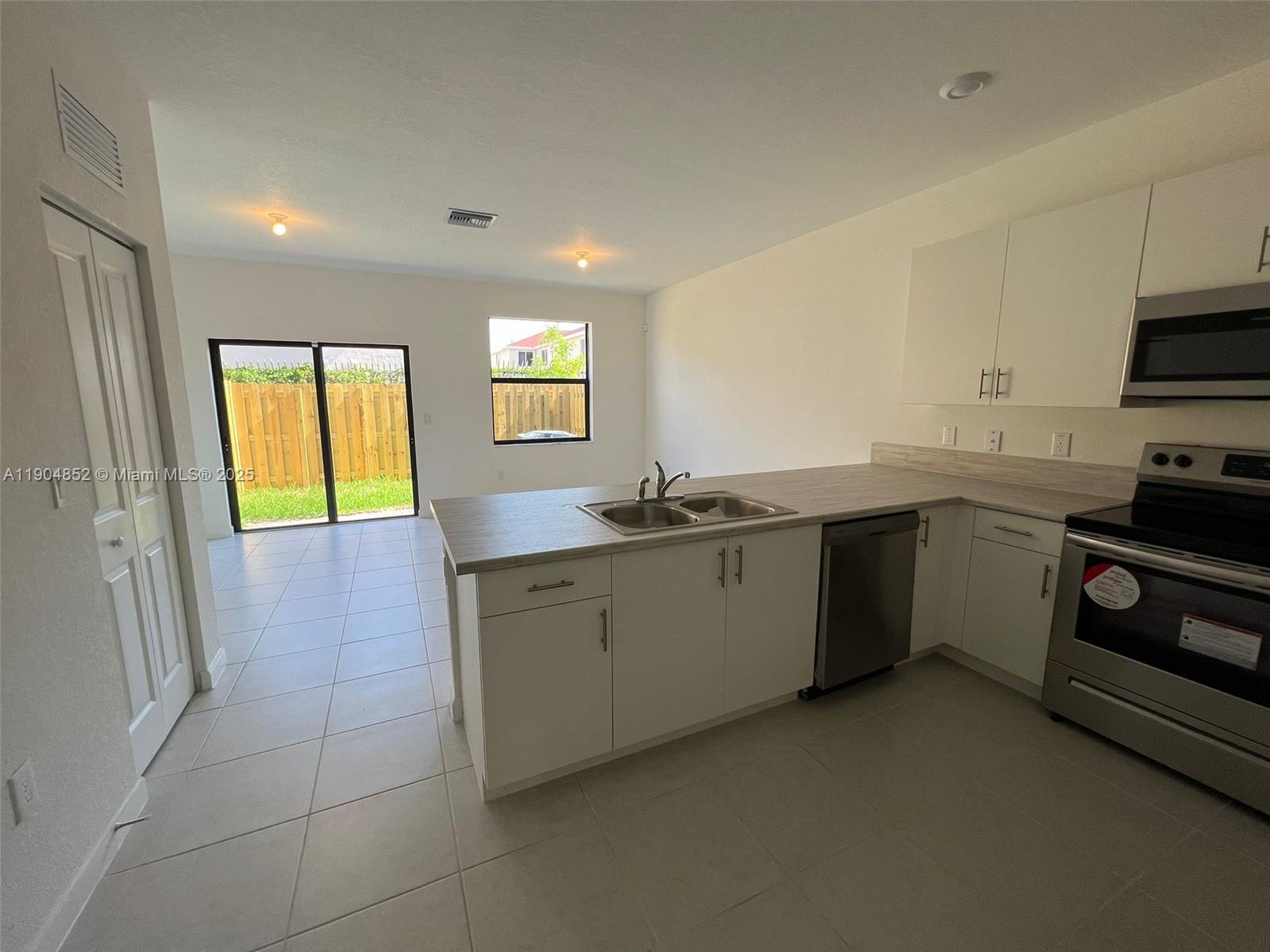 A kitchen with white cabinets, stainless steel appliances, and a sliding glass door to a yard — 875 NE 211TH ST # 0, Miami FL 33179, MIAMI, FL