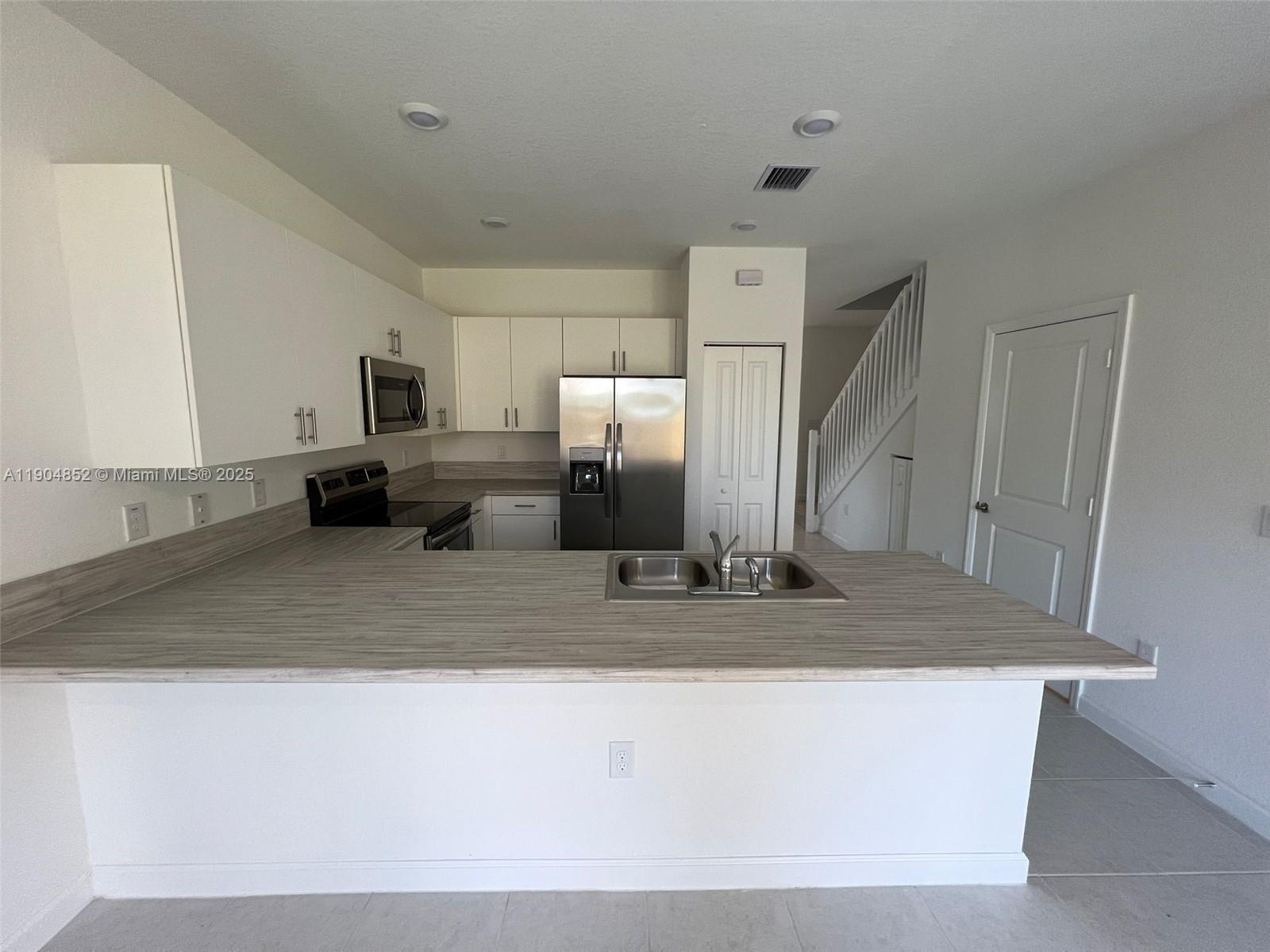 A kitchen features white cabinets, stainless steel appliances, and a wood-look laminate countertop island — 875 NE 211TH ST # 0, Miami FL 33179, MIAMI, FL