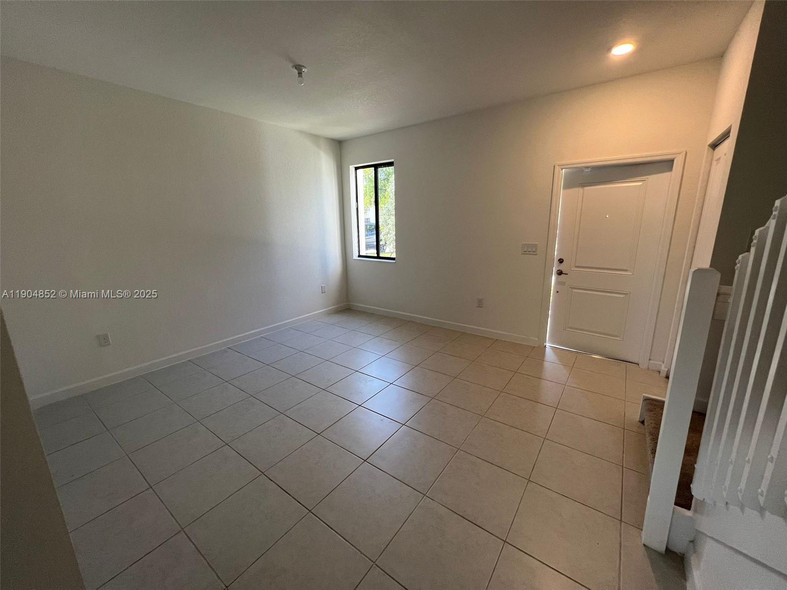 An empty room features light-colored tile flooring, white walls, a window, and a white door — 875 NE 211TH ST # 0, Miami FL 33179, MIAMI, FL
