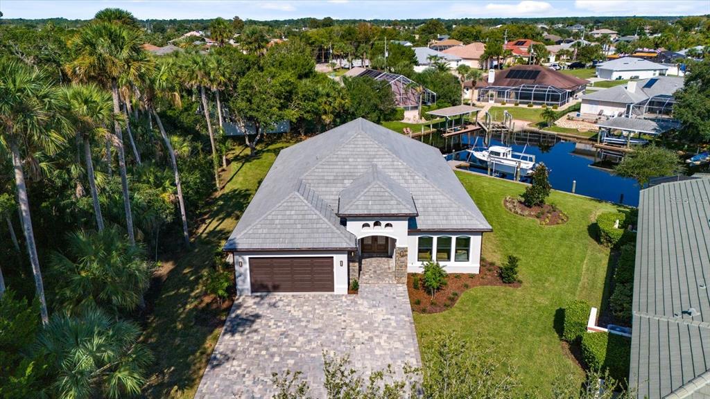 An aerial view shows a single-story house with a gray roof, paver driveway, and canal — 46 RIVERVIEW BEND N, PALM COAST, FL