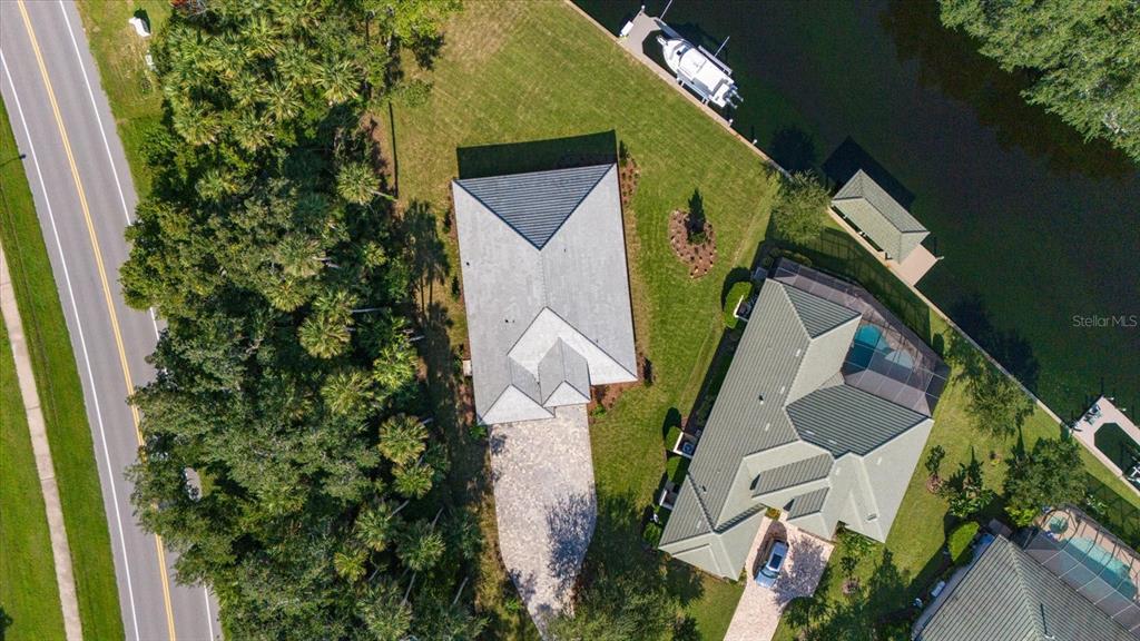 An aerial view shows two houses with metal roofs, paved driveways, and boat docks on a canal — 46 RIVERVIEW BEND N, PALM COAST, FL